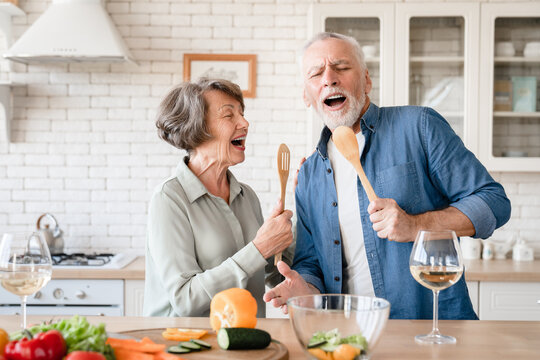Active seniors concept. Elderly senior old couple grandparents singing dancing at home kitchen while cooking dinner lunch, drinking wine and celebrating special event together