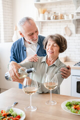 Fototapeta na wymiar Vertical shot of happy old elderly senior couple spouses grandparents celebrating special event anniversary Valentine`s day at home, drinking wine, having romantic dinner date in the kitchen
