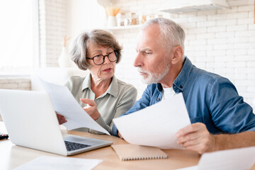 Concentrated concerned european senior old elderly couple spouses grandparents doing paperwork,...