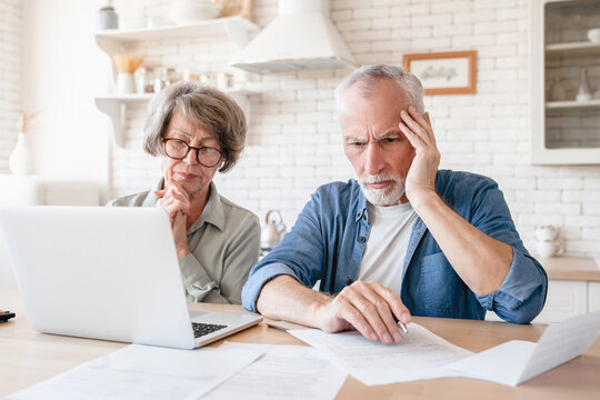 Depressed sad concentrated senior old elderly couple dealing with documents, solving financial problems, feeling confused while receiving mortgage loan contract at home kitchen - Powered by Adobe