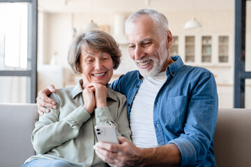Smart caucasian old elderly senior grandparents couple spouses using cellphone for scrolling social...
