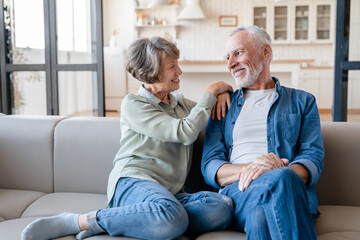 Cheerful caucasian senior old elderly couple spouses grandparents hugging embracing cuddling, spending time together while relaxing resting on the sofa couch - obrazy, fototapety, plakaty