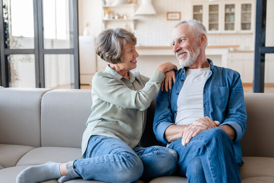 Cheerful caucasian senior old elderly couple spouses grandparents hugging embracing cuddling, spending time together while relaxing resting on the sofa couch