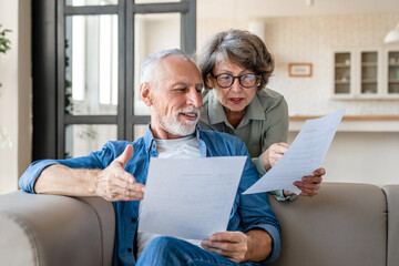 Mortgage loan debt transactions paying bills and documents. Caucasian senior old couple spouses reading marriage contract, doing paperwork, dealing with data at home - obrazy, fototapety, plakaty