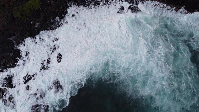 Aerial view captured by drone of large whitecap ocean waves in the Pacific ocean violently crashing into the rocky shore on the coast of Kauai in Hawaii at Spouting Horn.