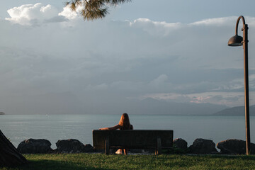 Lonely girl sits on a bench looking at the Lake Garda
