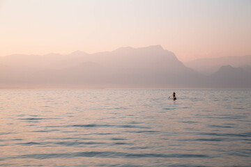 A lonely man standing on an inflatable board with an oar against a backdrop of misty mountains and a lake