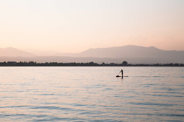 A lonely man standing on an inflatable board with an oar against a backdrop of misty mountains and a lake