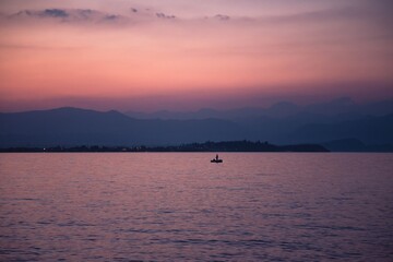A lonely fisher standing on an inflatable boat with an oar against a backdrop of misty mountains and a Garda lake