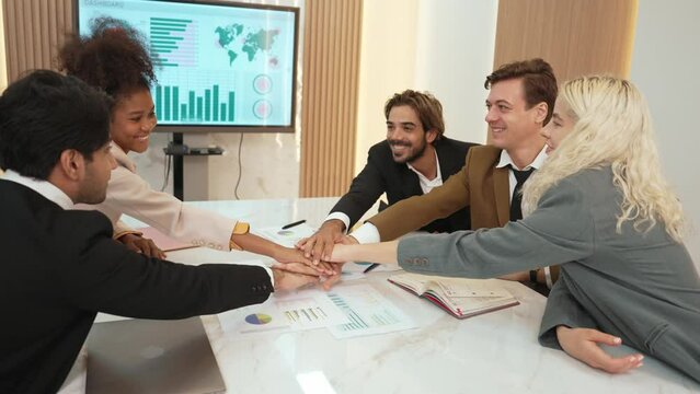 Group of diverse office worker join hand together in ornamented office room symbolize business synergy and strong productive teamwork in workplace. Cooperation and unity between business employee.