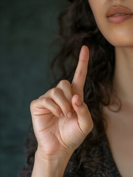 Woman raising hand and showing upwards direction, index finger extended up, closeup view of her hand, deaf person signing, speaker using sign language, asking a question, requesting permission