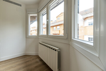 An empty room with a gallery full of windows with aluminum radiators