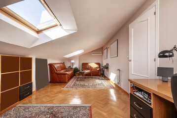 A large office in an attic room with skylights in the ceiling, a desk and a sofa