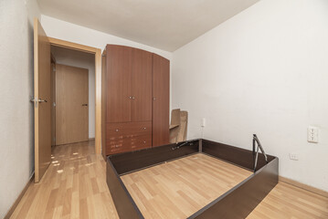 An empty room with white painted walls with gotelet, a large dismantled bed and a dark wooden wardrobe
