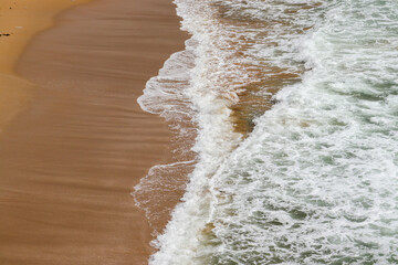 Moroccan atlantic sea waves with white foam on the sand.