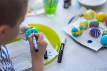 Close-up view of child drawing smiley face on colorfully decorated Easter egg. Sweden.