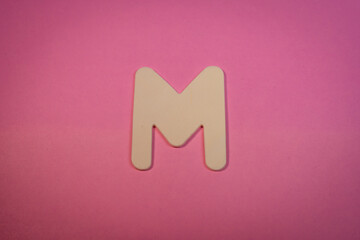 Letter M in wood on a pink background 