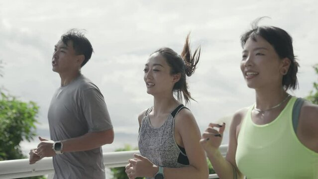 three young asian people running outdoors in park by the sea