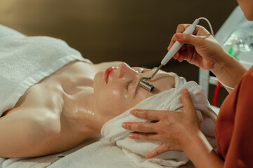 Obraz na płótnie Canvas Beautiful young women lie on spa bed while having facial massage from professional doctor. Attractive female with beautiful skin surrounded by electric facial machine. Tranquility.