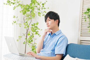 自宅でノートパソコンを使いながら考える男性