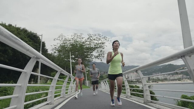 rear view of three young asian people running outdoors in park	