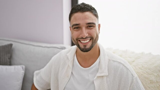 Cheeky young arab man perfectly winking at camera, giving a sexy wink from his living room sofa. his happy face beacons joy while oozing handsome charm, inducing laughter. home never looked this cool!