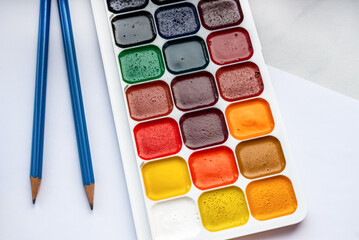 Colorful watercolor or acrylic paints and pencils on a white sheet of paper on a white background. Design studio table top view. 