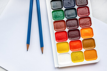 Colorful watercolor or acrylic paints and pencils on a white sheet of paper on a white background. Design studio table top view. 