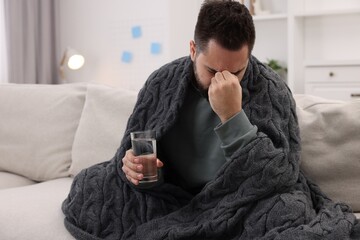 Man with glass of water suffering from headache on sofa at home