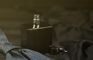 A bottle of mens cologne and cufflinks with blue tie lie on a black luxury fabric background on a...