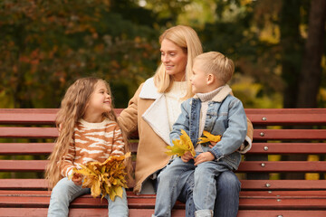 Happy mother and her children spending time together with dry leaves in autumn park