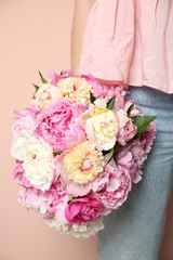 Woman with bouquet of beautiful peonies on beige background, closeup