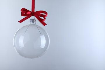 Transparent glass Christmas ball with red ribbon and bow against light background. Space for text