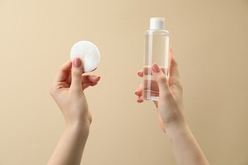 Woman holding makeup remover and cotton pad on beige background, closeup