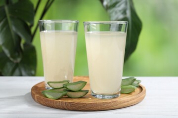 Fresh aloe juice in glasses and cut leaves on white wooden table outdoors