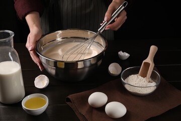 Woman making dough with whisk in bowl at table, closeup