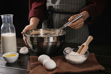 Woman making dough with whisk in bowl at table, closeup