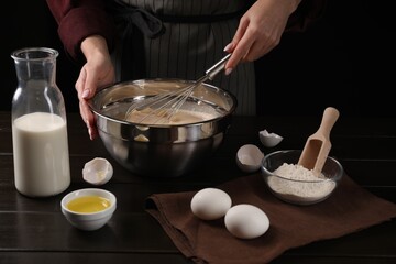 Woman making dough with whisk in bowl at table, closeup
