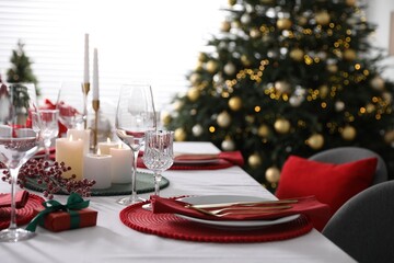 Christmas table setting with burning candles, gift box and dishware indoors