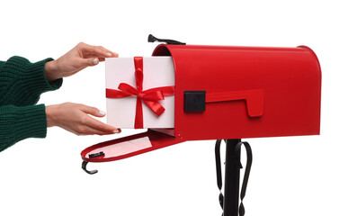 Woman putting Christmas gift into mailbox on white background, closeup. Sending present by mail