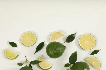 Limes and green leaves on white background, flat lay. Space for text