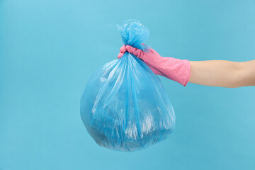 Woman holding plastic bag full of garbage on light blue background, closeup - obrazy, fototapety, plakaty