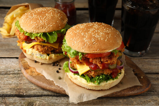 Delicious burgers with crispy chicken patty, french fries and soda drinks on wooden table