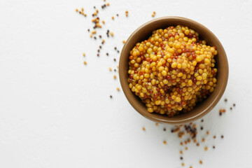 Fresh whole grain mustard in bowl and dry seeds on white table, flat lay. Space for text