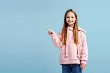 Smiling attractive little girl wearing stylish casual clothes pointing finger to copy space