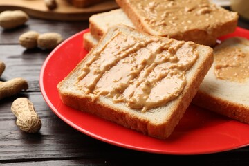 Delicious toasts with peanut butter on dark wooden table, closeup