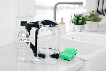 Cleaning electric kettle. Bottle of vinegar, sponge and baking soda on countertop in kitchen