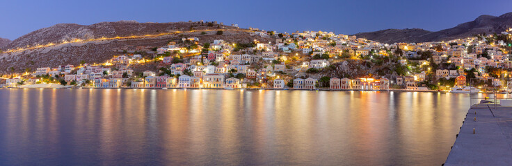 Fototapeta na wymiar Multi-colored facades of houses in the light of lanterns in the village of Symi at sunset.