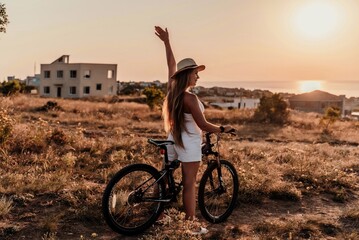 A woman cyclist on a mountain bike looking at the landscape sea. Adventure travel on bike. - obrazy, fototapety, plakaty
