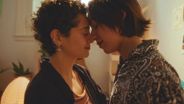 Young loving lesbian couple rubbing noses with eyes closed and admiring each other during romantic moment at home